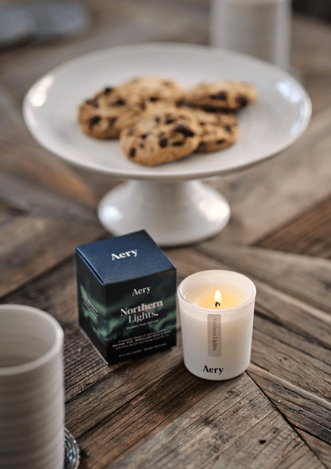 Candle with 'Aery' packaging on a wooden table with cookies in the background