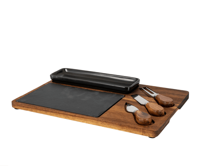 Wooden cutting board with black stone, small black pan, and wooden-handled knives on a white background