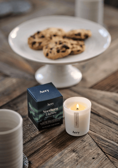 Candle with 'Aery' packaging on a wooden table with cookies in the background