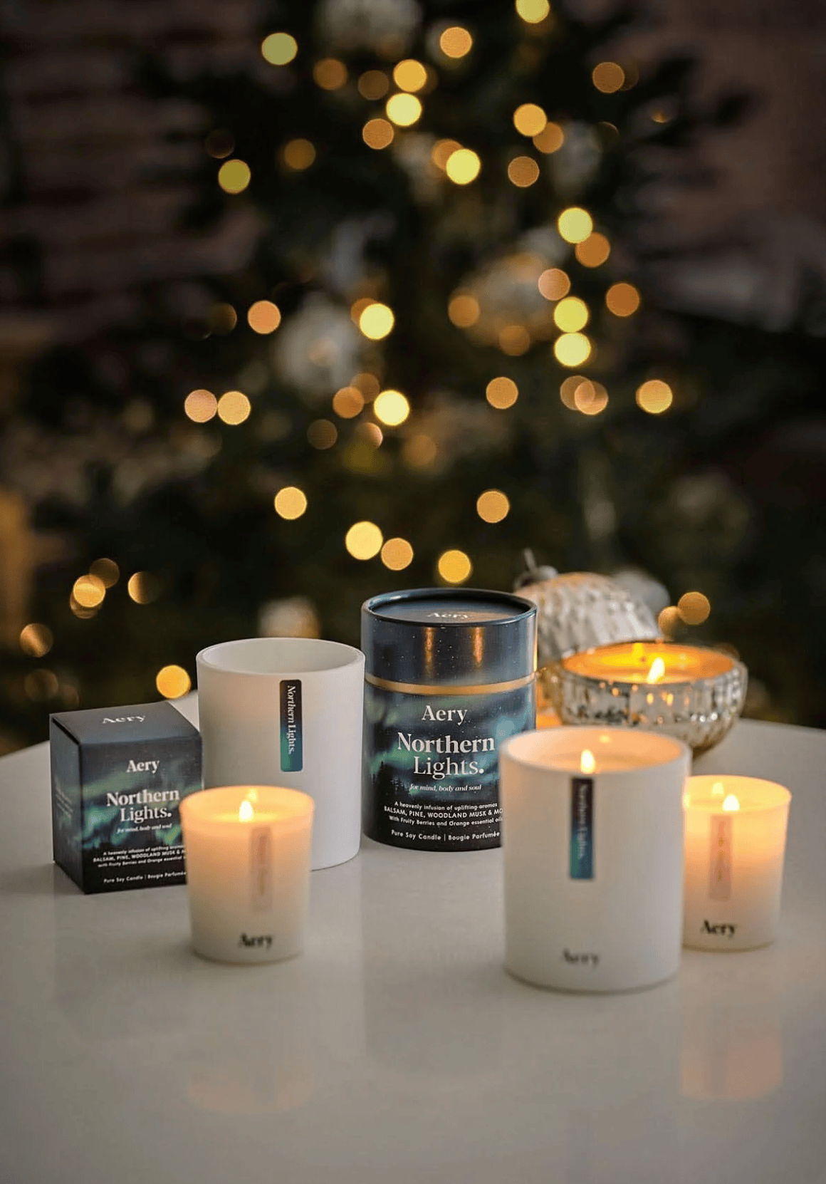 Aery candles and packaging on a table with a blurred Christmas tree in the background