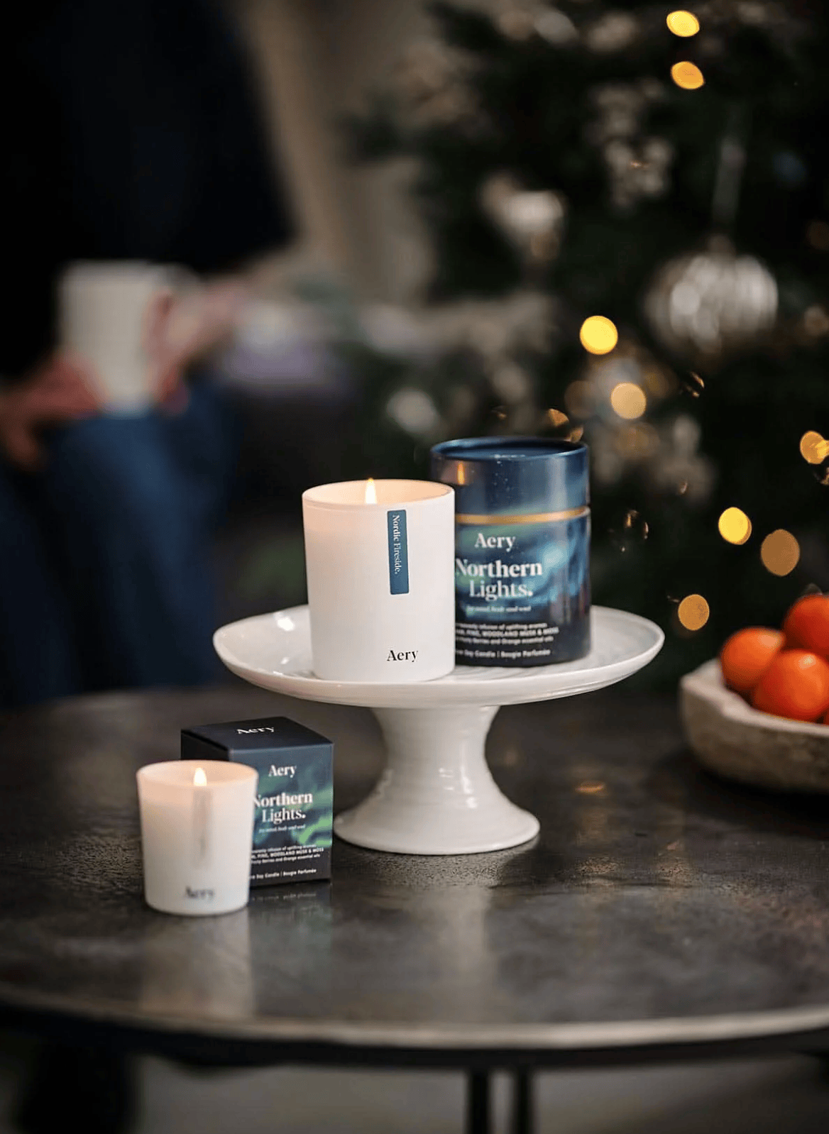 Aery candles and packaging on a table with a blurred Christmas tree in the background