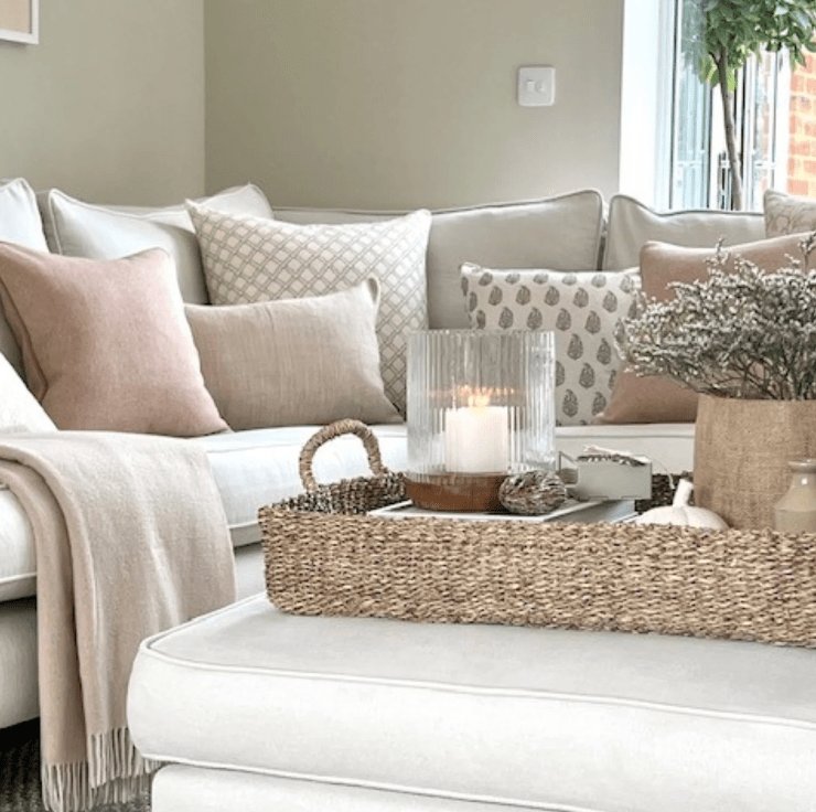 Cozy living room with a white sofa, decorative pillows, and a woven basket on an ottoman.