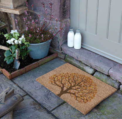 Doormat with tree design on a stone pathway with milk bottles and plants.