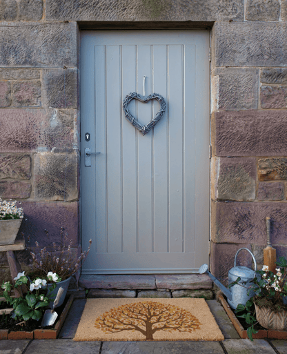 Gray front door with a heart-shaped wreath on a stone wall, surrounded by plants and decor.