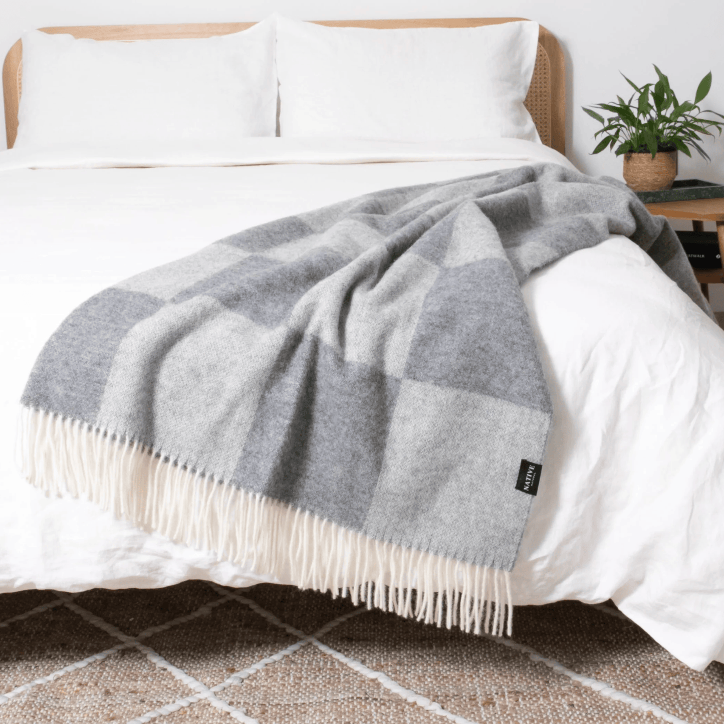 Grey checkered blanket on a bed with white pillows and a plant in the background.