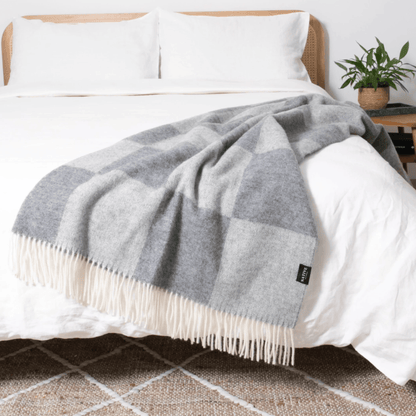 Grey checkered blanket on a bed with white pillows and a plant in the background.