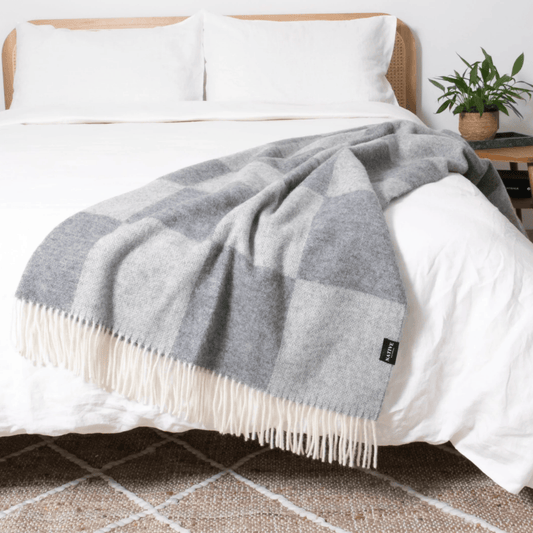 Grey checkered blanket on a bed with white pillows and a plant in the background.