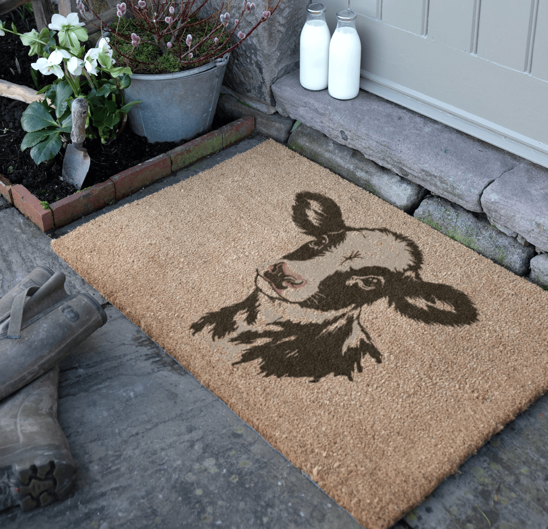 Doormat with a dairy calf design on a stone pathway, with plants and milk bottles in the background.