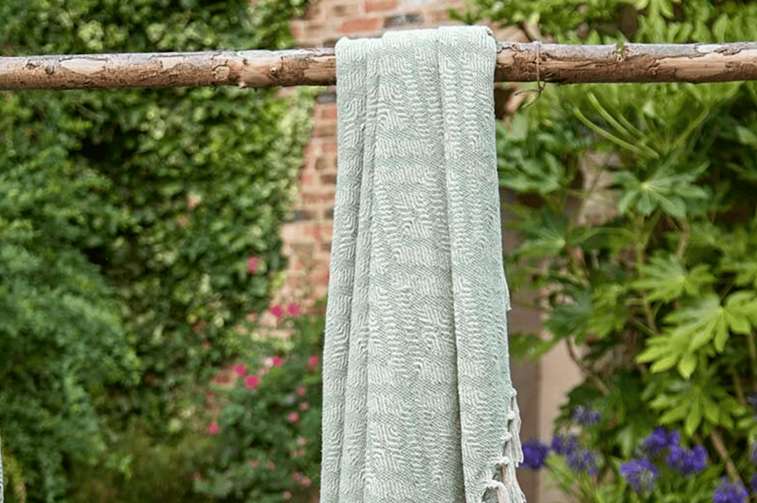 Light green fabric hanging on a wooden stick against a garden background