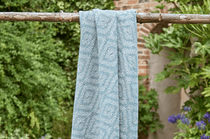 Blue textured towel hanging on a wooden stick with greenery and a building in the background