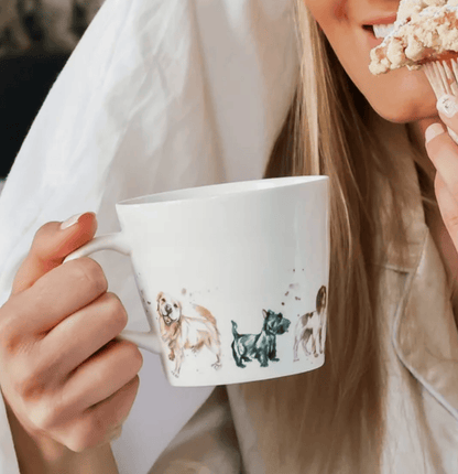 Person holding a mug with dog illustrations and eating a cupcake.