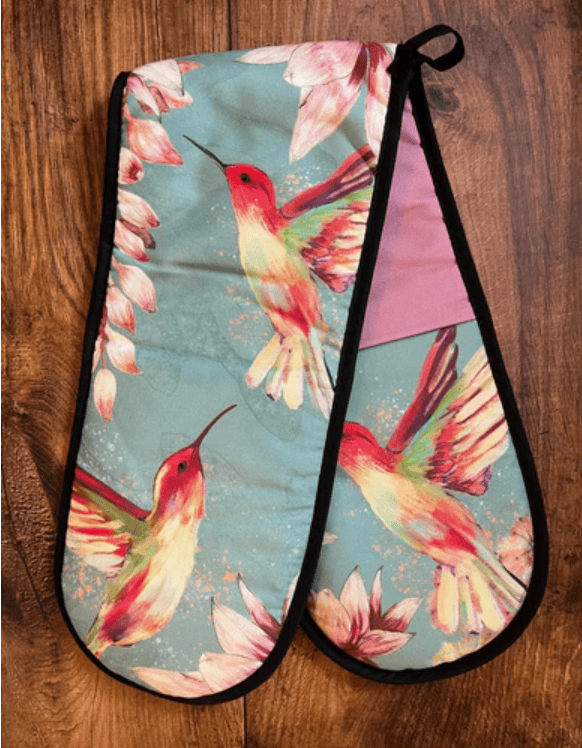 Pair of oven mitts with hummingbird and floral design on a wooden surface
