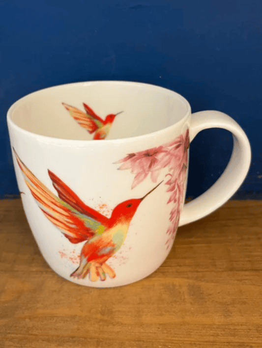 White mug with hummingbird design on a wooden surface and blue background