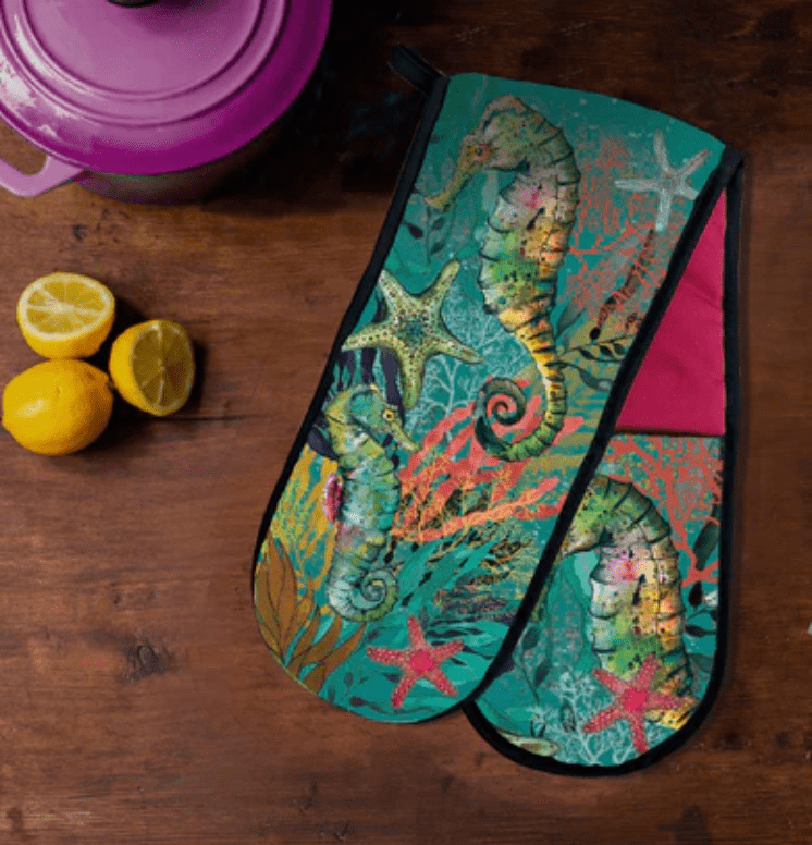 Colorful oven mitt with sea-themed design on a wooden surface with lemons and a purple pot.