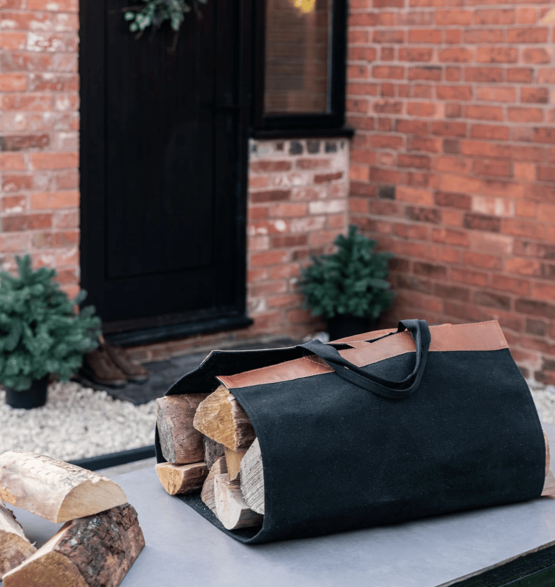 Black and brown log carrier with logs on a patio in front of a brick wall.