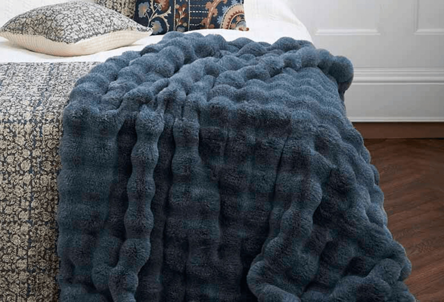 Blue textured blanket draped over a bed in a bedroom setting