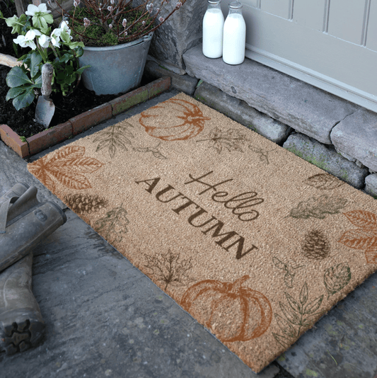 Doormat with autumn design and 'Hello Autumn' text on a stone porch.
