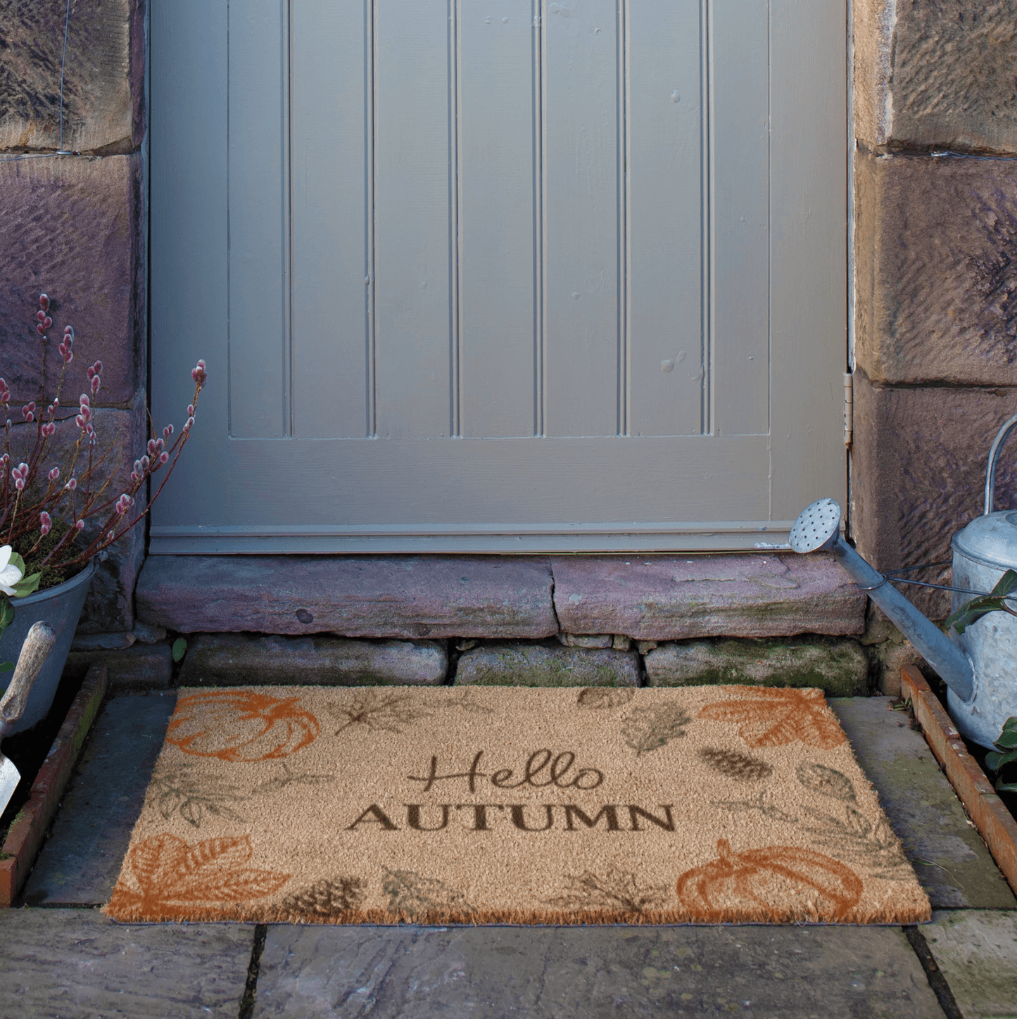 Doormat with 'Hello Autumn' text in front of a door on a stone path.