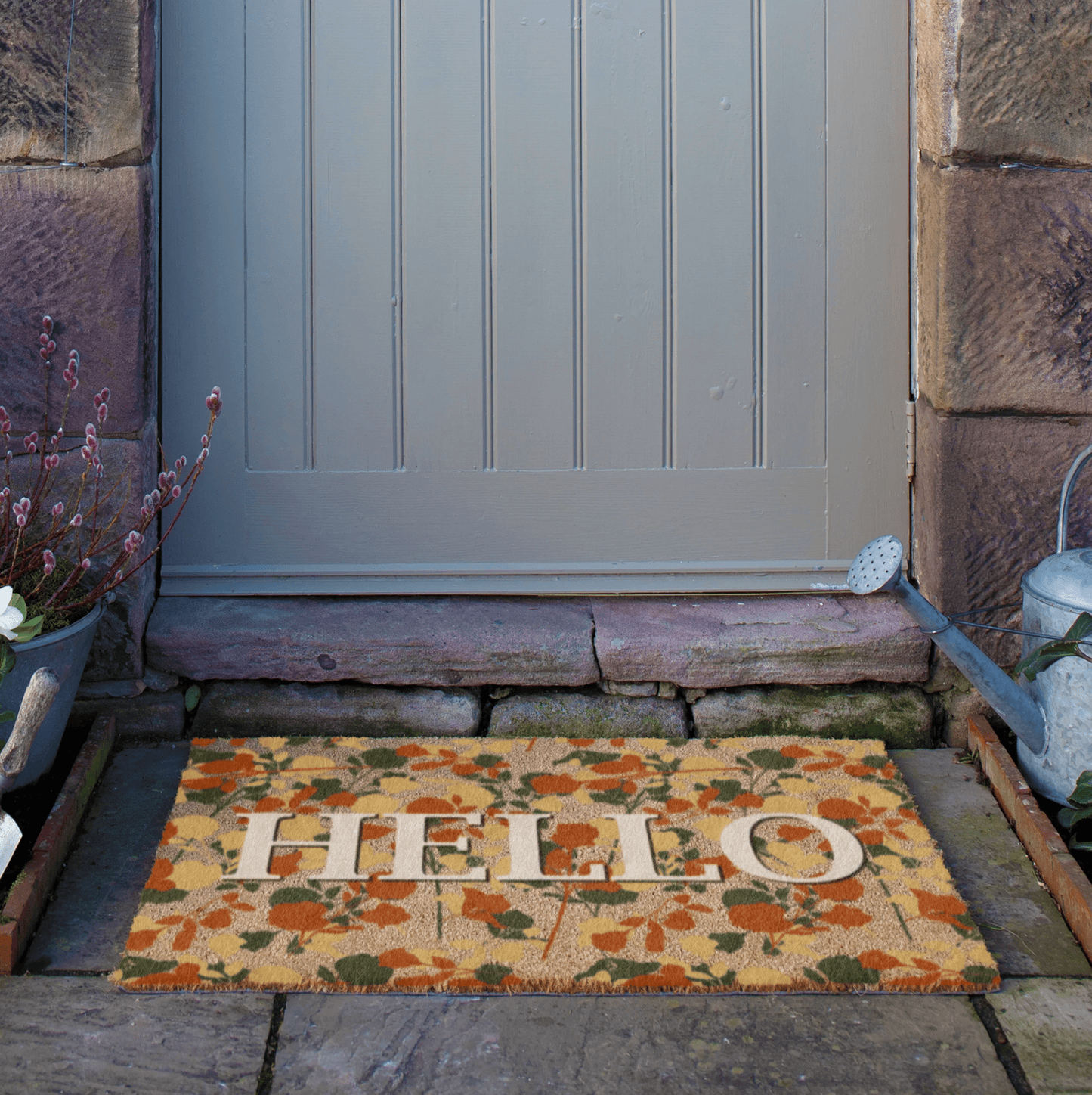 Doormat with 'HELLO' on a stone pathway leading to a door.