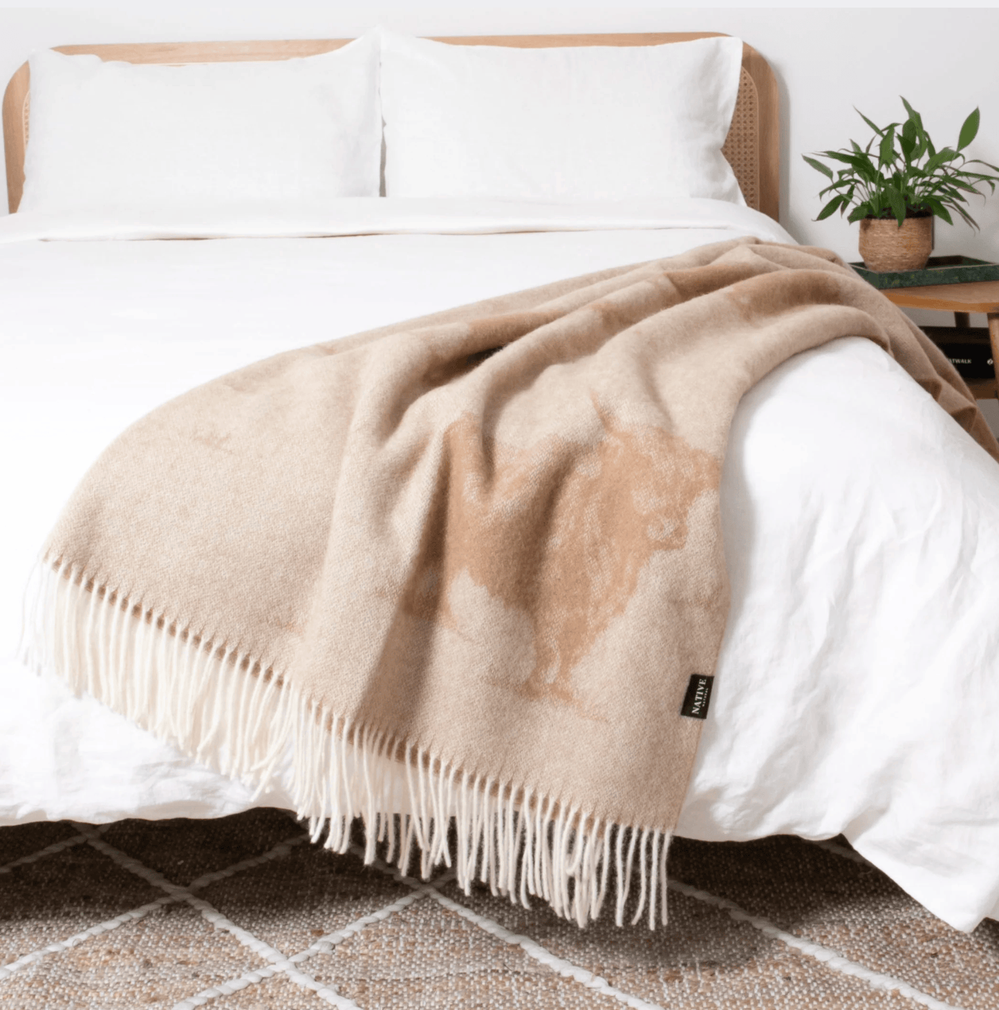 Beige Highland Cow throw blanket on a bed with white bedding and a plant in the background.