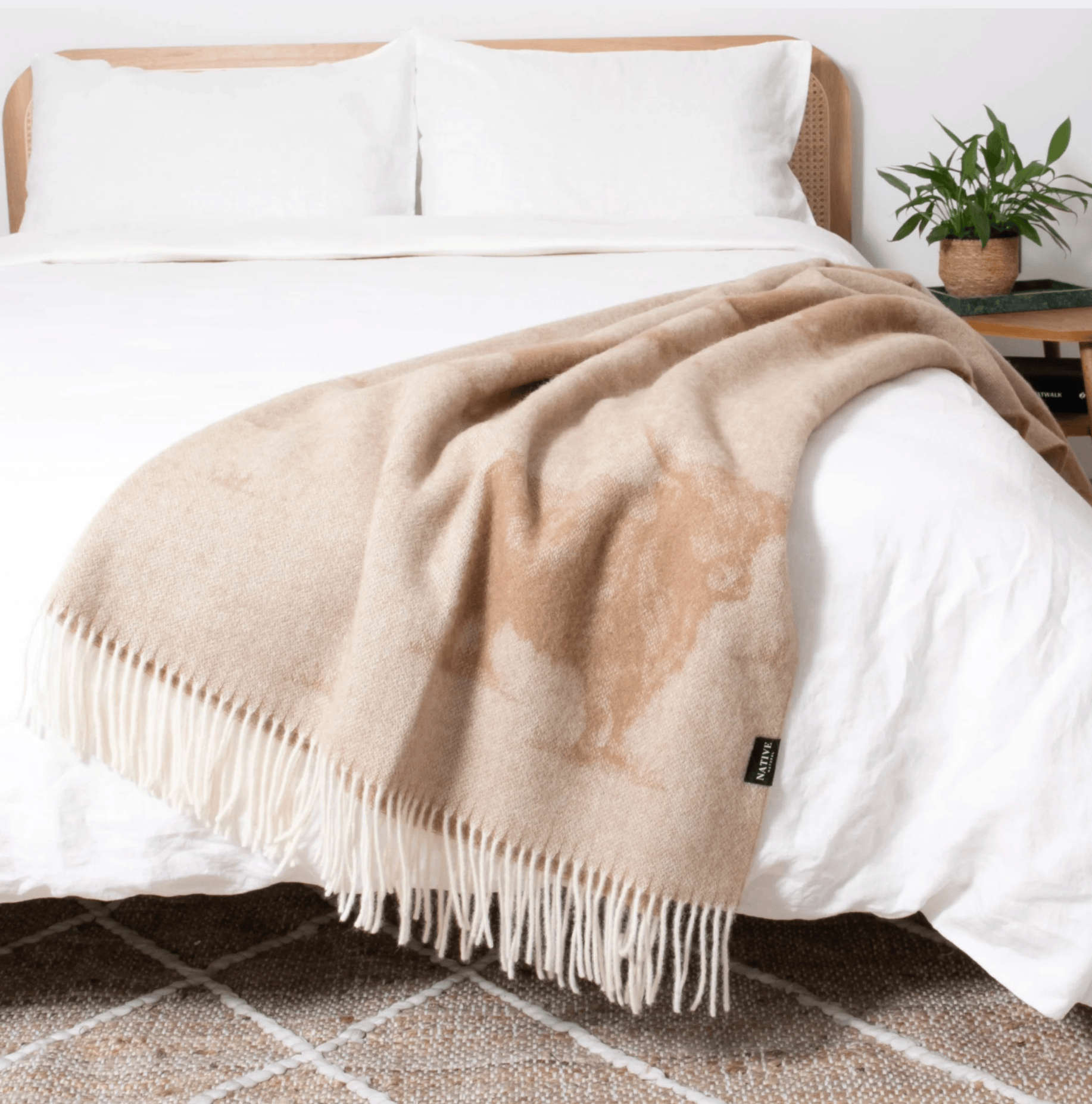 Beige Highland Cow throw blanket on a bed with white bedding and a plant in the background.