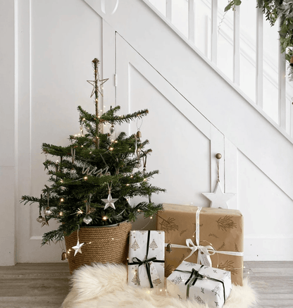 Small decorated Christmas tree with lights and ornaments, surrounded by wrapped gifts in a home setting.
