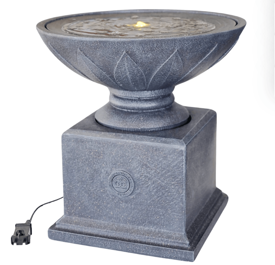 A gray stone-look outdoor fountain with a square pedestal base, a lotus-shaped bowl, and a small glowing flame effect visible in the water. A power cord is attached at the lower left, photographed on a plain white background.