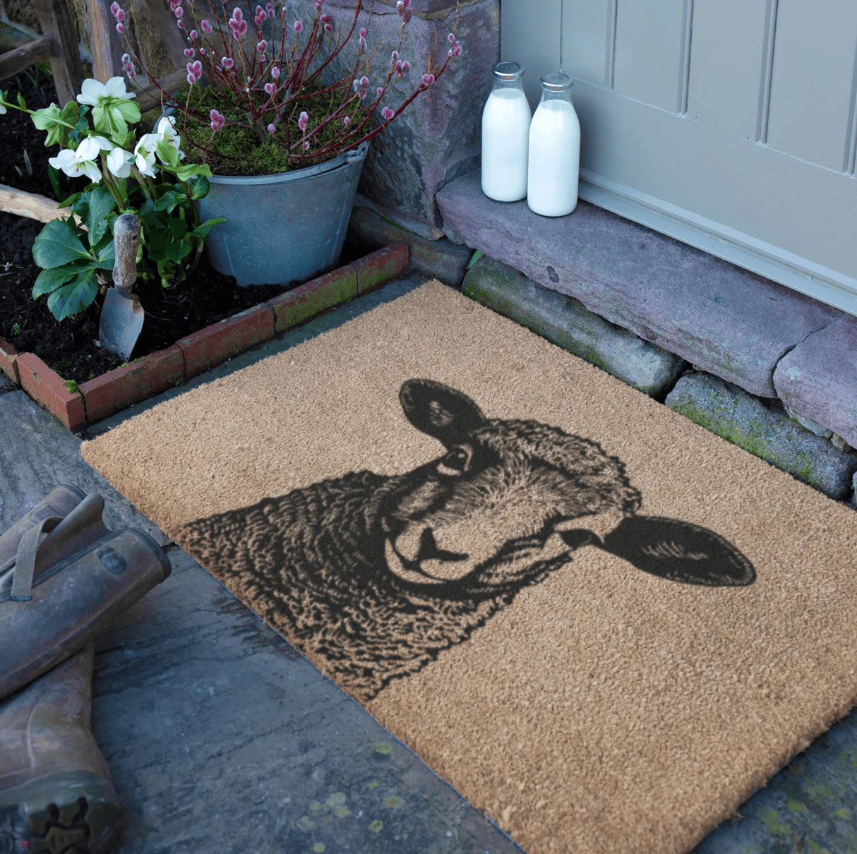 Doormat with Lamb design on a stone porch with plants and milk bottles.
