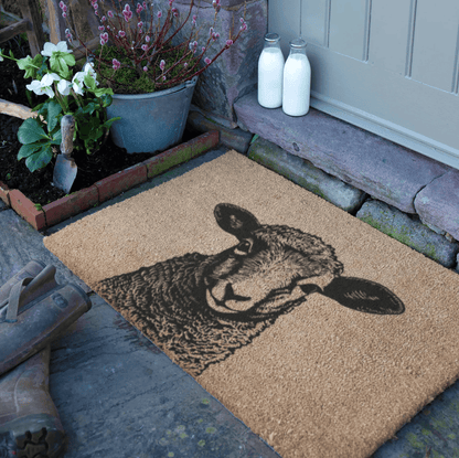 Doormat with Lamb design on a stone porch with plants and milk bottles.