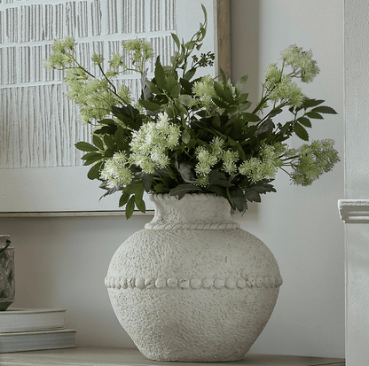 Decorative vase with greenery on a shelf against a neutral wall.