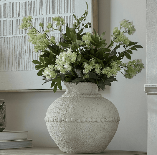 Decorative vase with greenery on a shelf against a neutral wall.