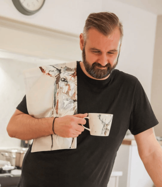 Man holding a tea towel and mug with Meg Hawkins Stag design in a kitchen setting