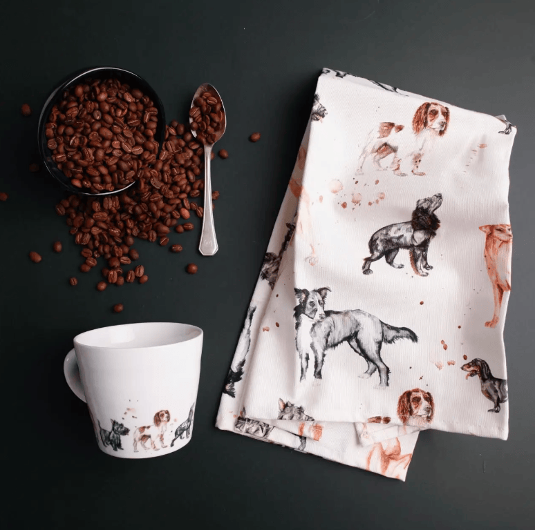 Tea towel with dog pattern next to a mug and coffee beans on a dark surface