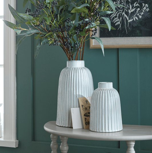 Two white textured vases on a table against a green wall with a framed picture.