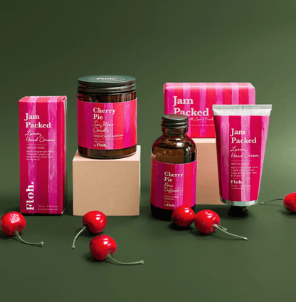 Collection of 'Jam Packed' skincare products with cherry-themed packaging on a green background.
