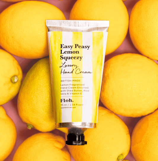 Hand cream tube labeled 'Easy Peasy Lemon Squeezy' surrounded by lemons on a pink background