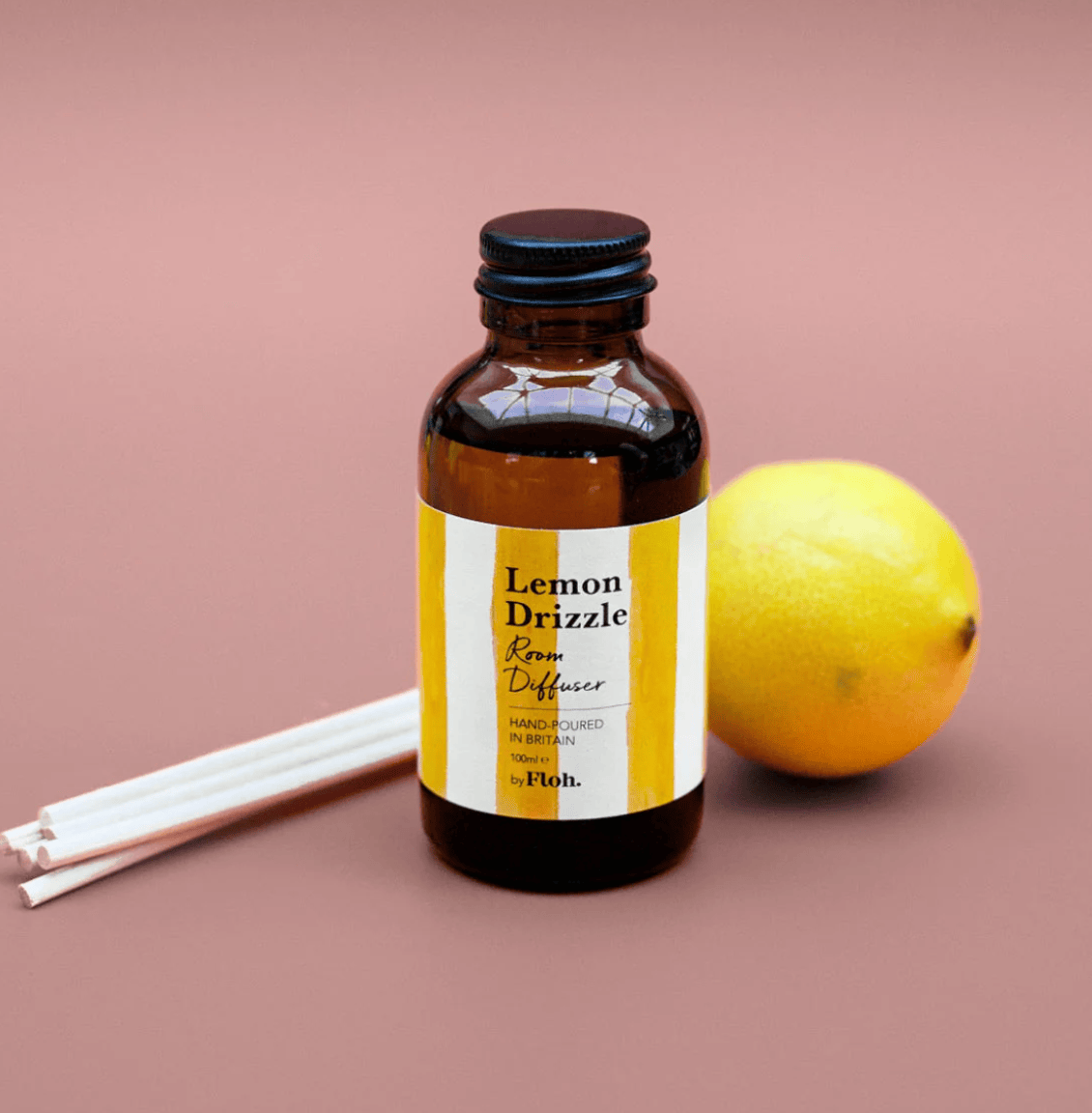 Bottle of Lemon Drizzle room diffuser with a lemon and sticks on a pink background