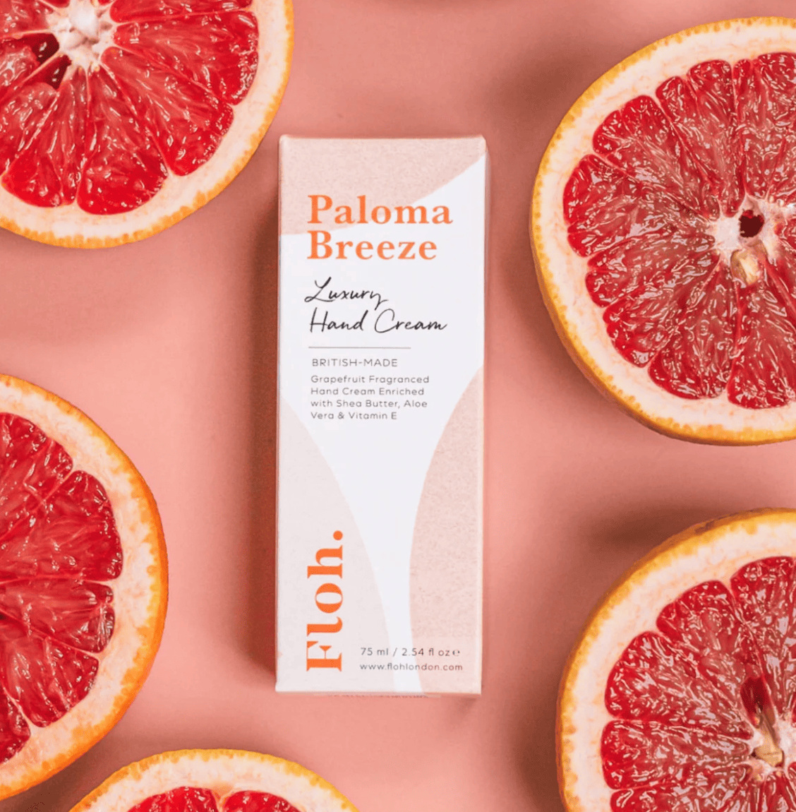 Paloma Breeze hand cream box surrounded by sliced grapefruits on a pink background