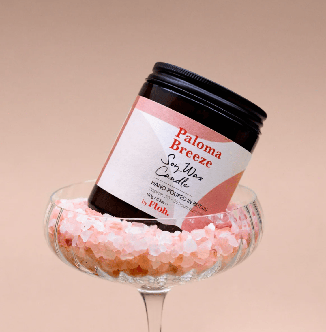 Jar of Palona Breeze soy wax candle with a decorative glass base filled with pink crystals on a beige background.
