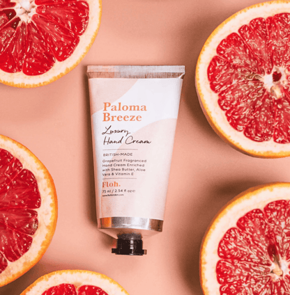 Paloma Breeze hand cream tube surrounded by sliced grapefruits on a beige background