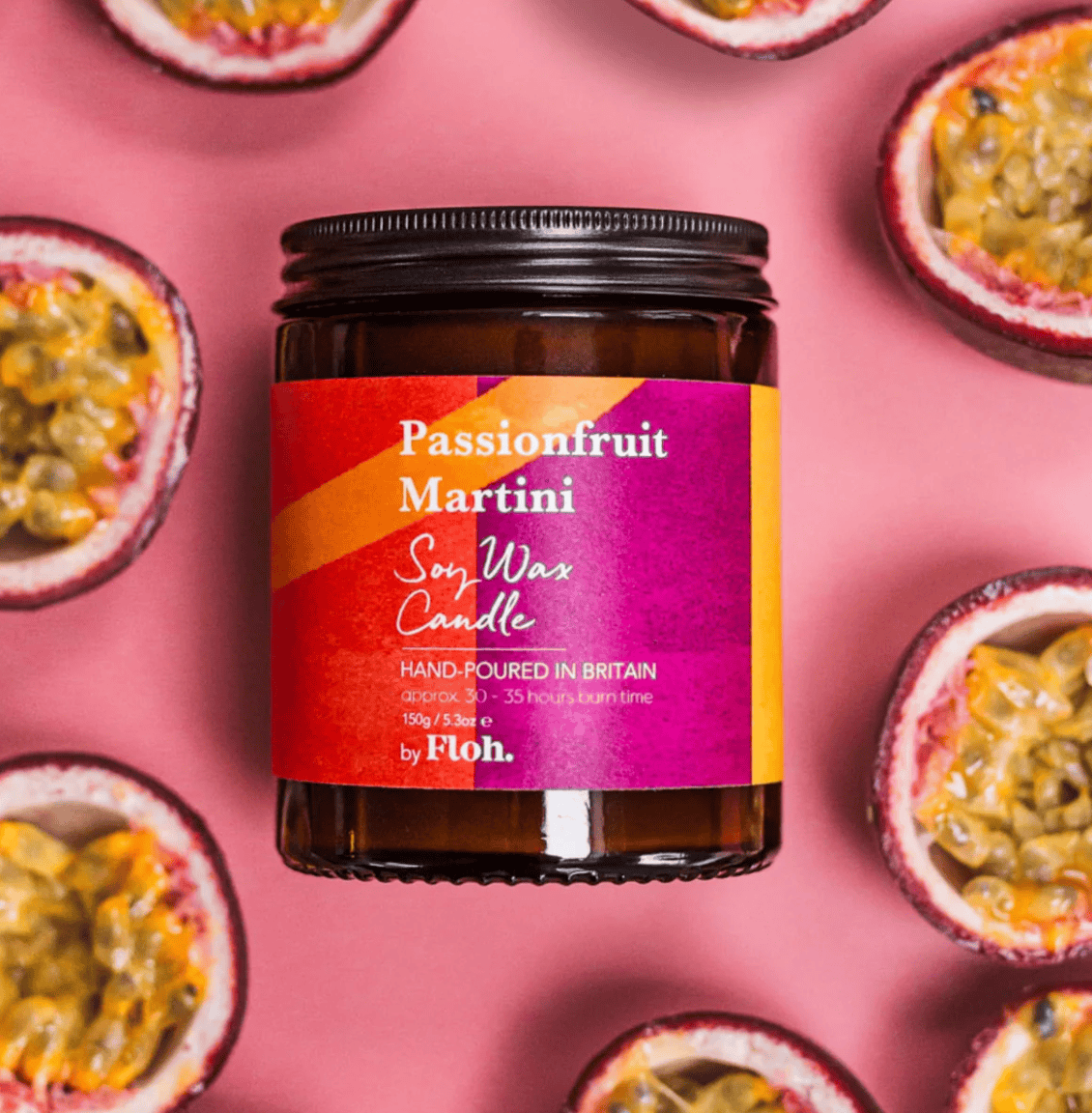 Passionfruit Martini soy wax candle jar with a colorful label on a pink background with passionfruit halves.