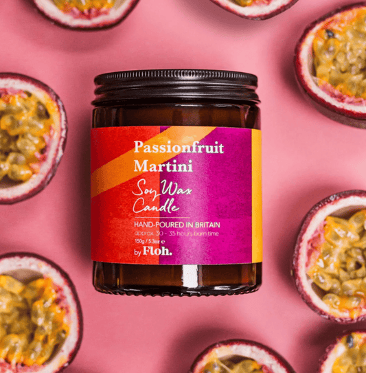 Passionfruit Martini soy wax candle jar with a colorful label on a pink background with passionfruit halves.
