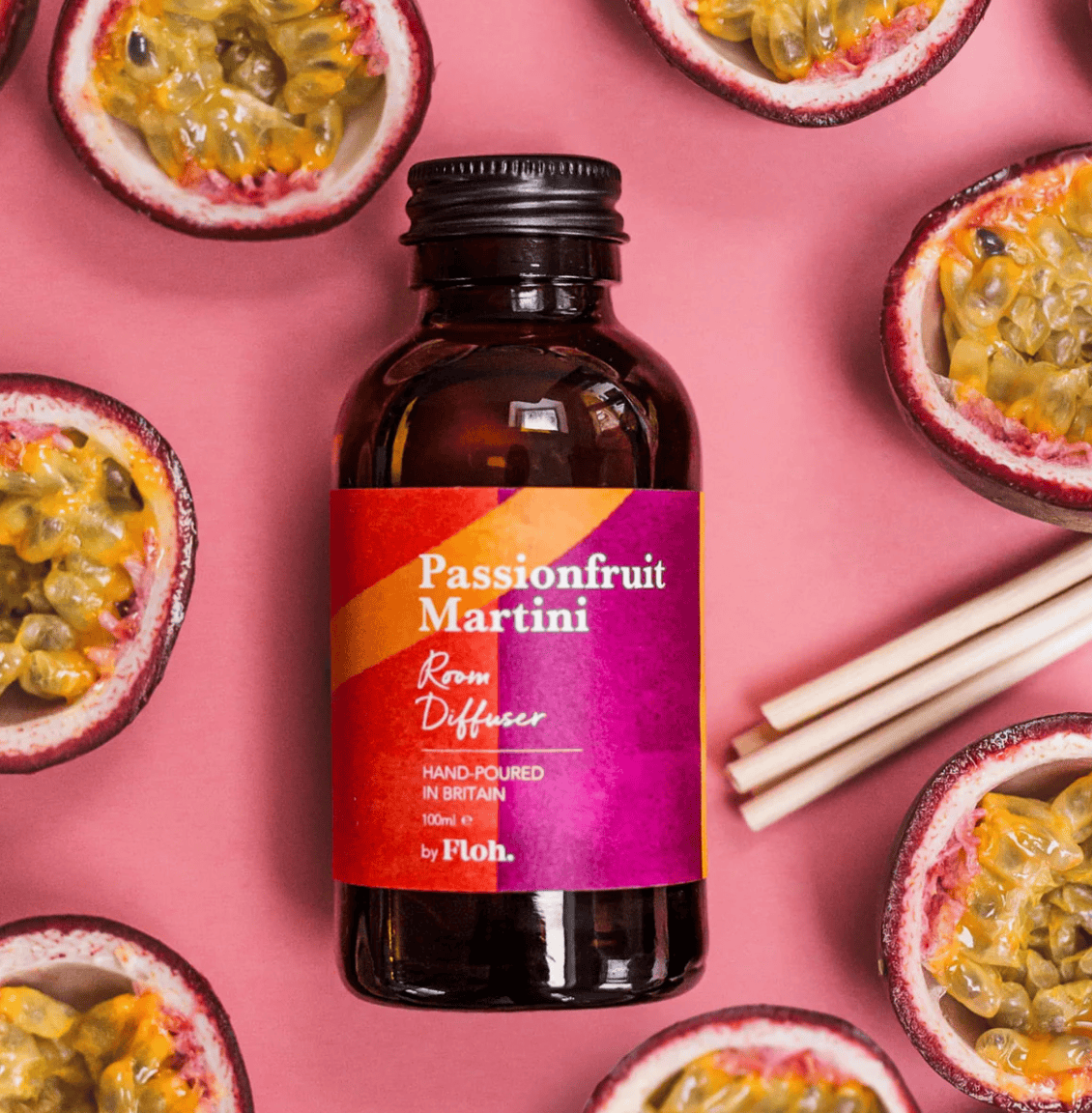 Bottle of Passionfruit Martini diffuser surrounded by passionfruit halves on a pink background