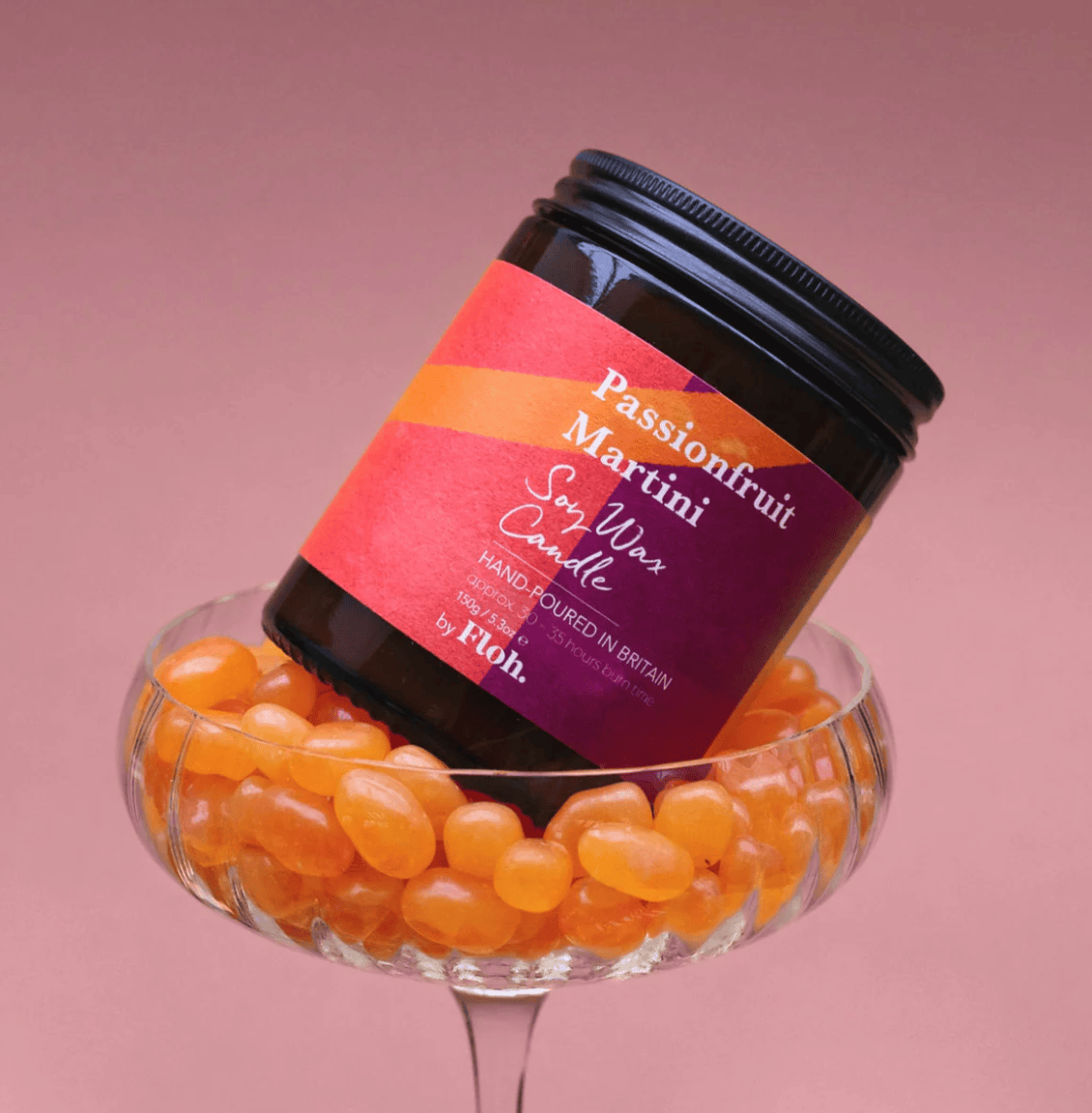 Passionfruit Martini soy wax candle in a glass container filled with passionfruit candies on a pink background.