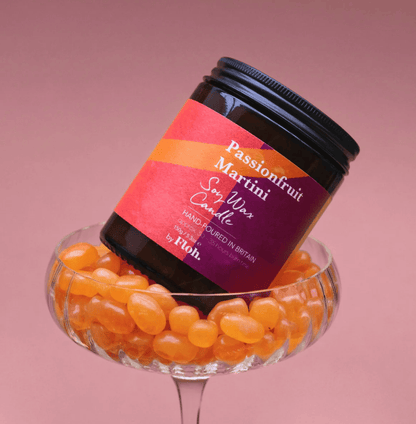 Passionfruit Martini soy wax candle in a glass container filled with passionfruit candies on a pink background.