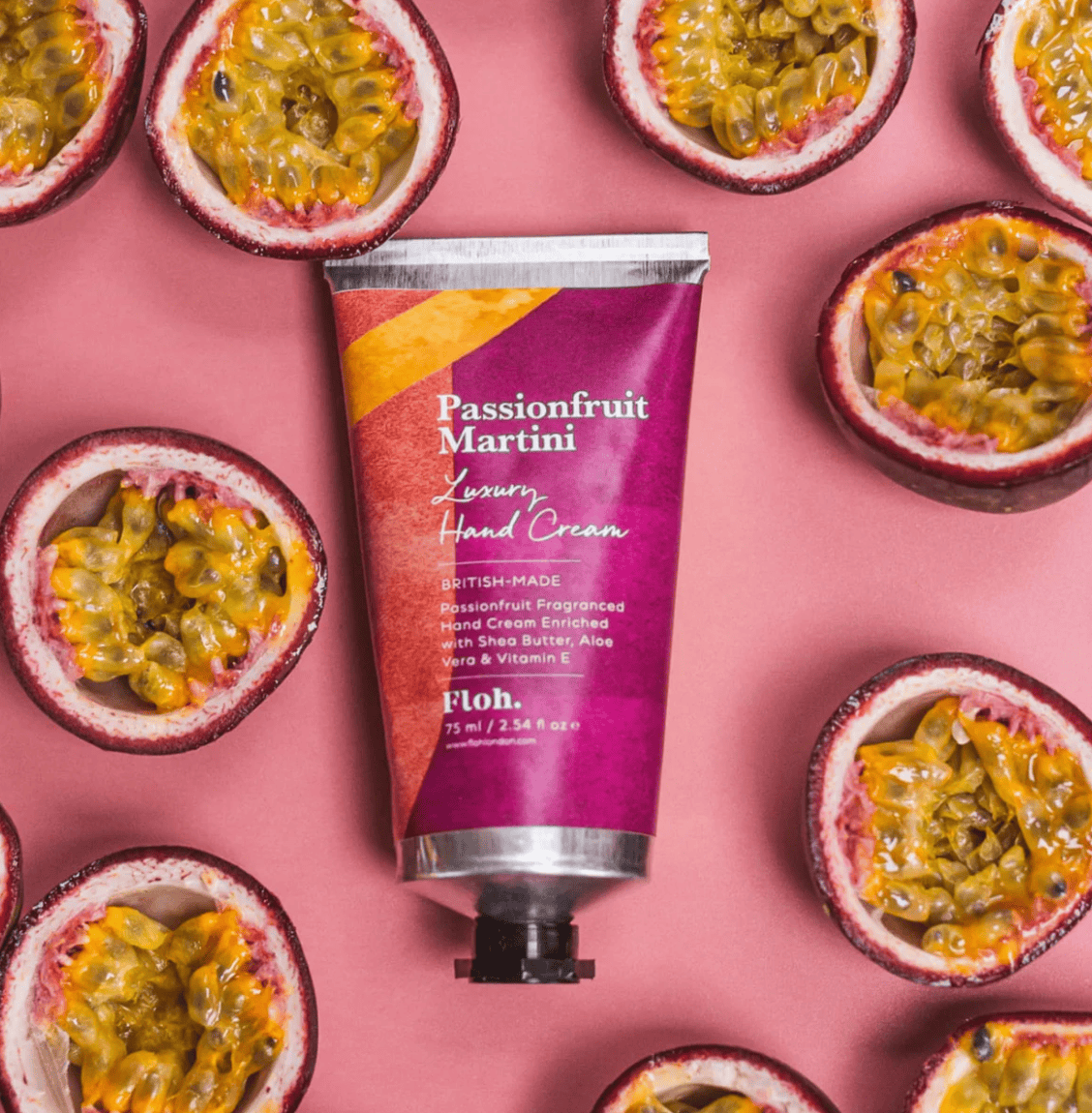 Hand cream tube labeled 'Passionfruit Martini' surrounded by passionfruit halves on a pink background