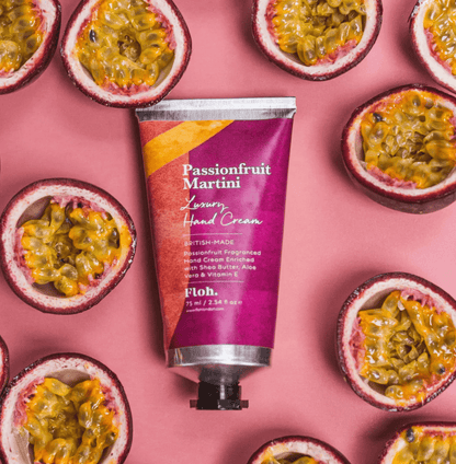 Hand cream tube labeled 'Passionfruit Martini' surrounded by passionfruit halves on a pink background