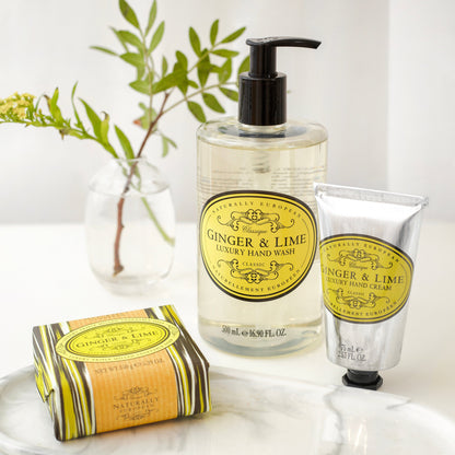 Somerset Toiletries Ginger & Lime luxury hand wash, cream, and soap on a white surface with greenery in the background.