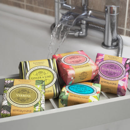 Five Somerset Toiletries Naturally European soap bars with colourful packaging on a sink, water flowing in the background