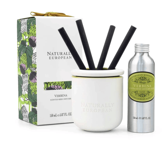 Naturally European Verbena scented reed diffuser set with a white ceramic diffuser bowl, four black reeds, a silver atomizer bottle, and its illustrated green and white box.